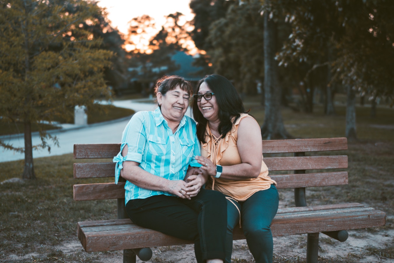 Woman and mother sitting and laughing on a park bench at sundown